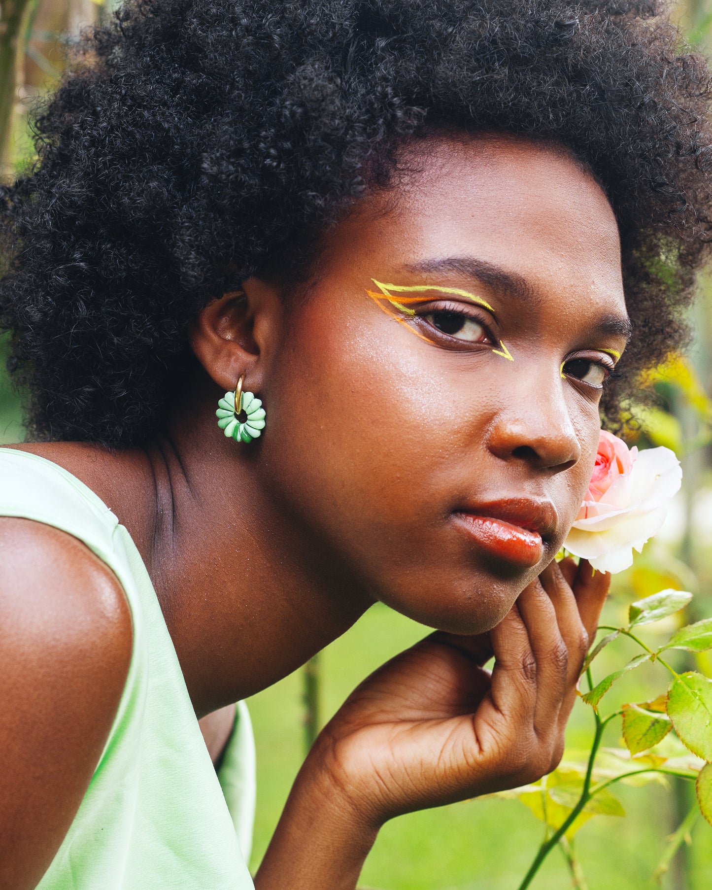 visage de femme noire de profil, portant deux boucles d'oreilles en argile polymère faites mains, en forme de fleur de marguerite, vertes dégradées, montées sur des anneaux ronds dorés en acier inoxydable
