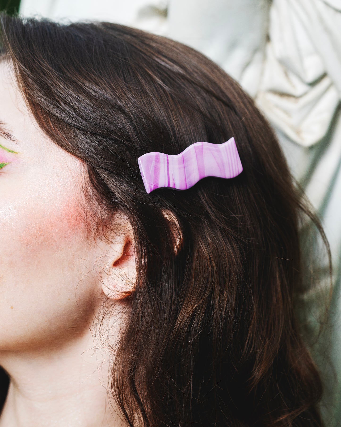 visage de femme brune devant une statue antique portant une barrette à cheveux violette marbrée avec pince crocodile, de forme en vague, rétro
