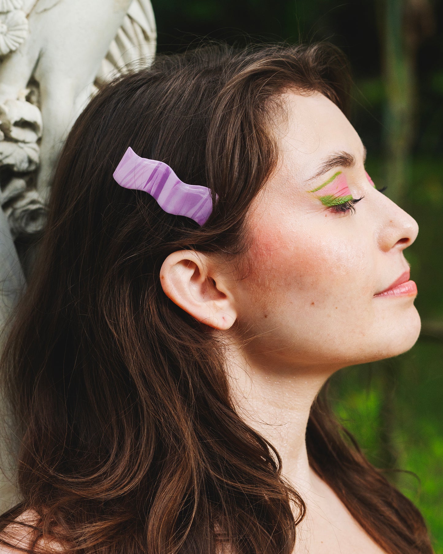 visage de profil de femme brune devant une statue antique portant une barrette à cheveux violette marbrée avec pince crocodile, de forme en vague, rétro