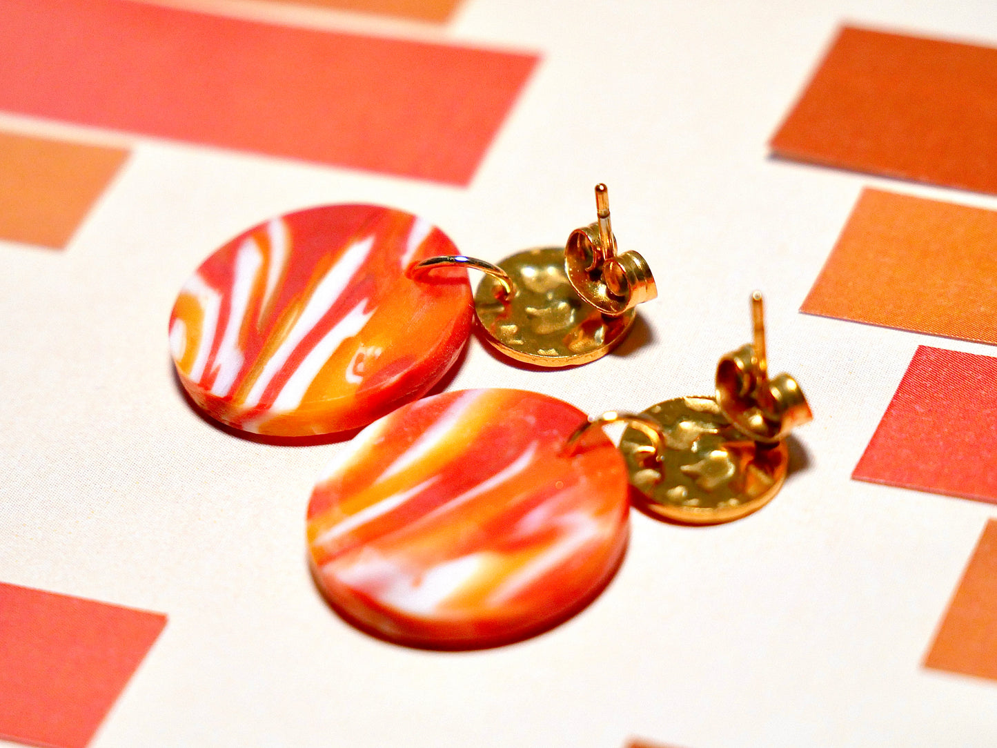 paire de boucles d'oreilles montrant la face arrière des bijoux et leurs attaches. Elles sont en argile polymère rondes surmontées d'un apprêt rond bosselé doré en acie