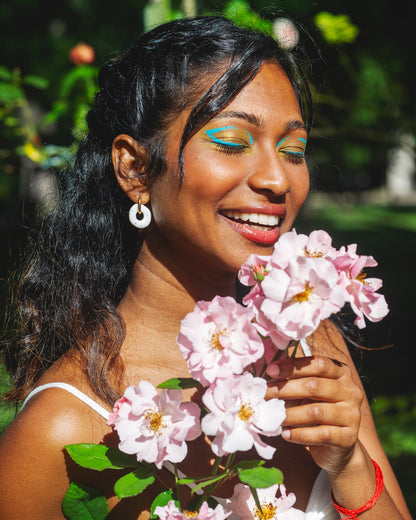 femme indienne souriant qui tient des hortensias roses et porte une boucle d'oreille ronde en argile polymère faite main blanche avec des points noirs incrustés, avec un anneau doré en acier inoxydable