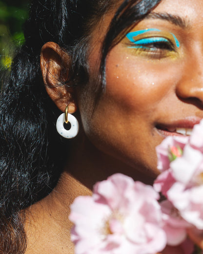 visage de femme indienne de profil qui tient des hortensias roses et porte une boucle d'oreille ronde en argile polymère faite main blanche avec des points noirs incrustés, avec un anneau doré en acier inoxydable