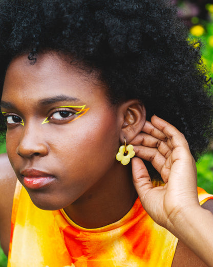 visage de femme noire portant une boucle d'oreille fantaisie faite main en forme de fleur jaune, avec un anneau en acier inoxydable