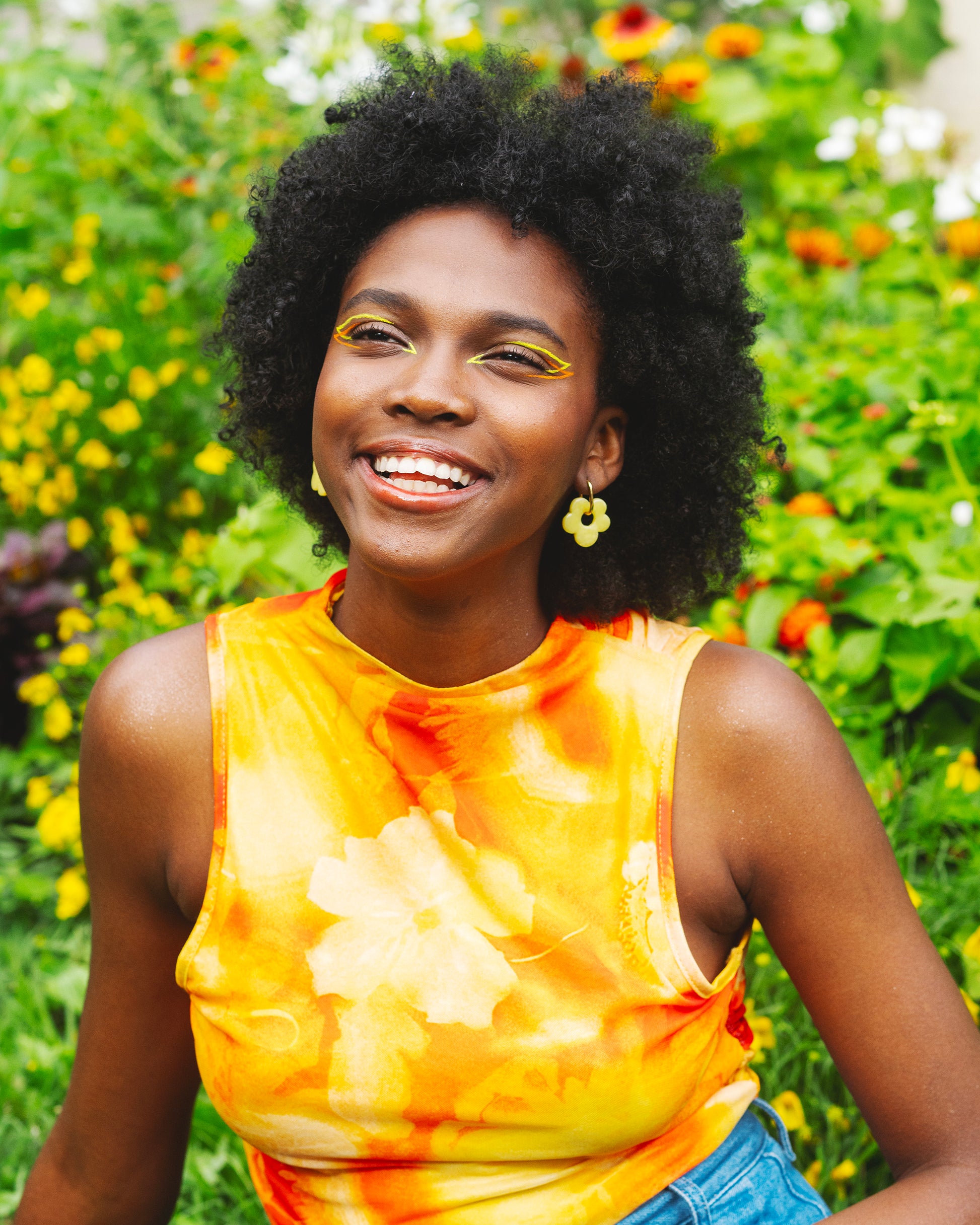 femme noire souriant dans un jardin et portant une boucle d'oreille fantaisie faite main en forme de fleur jaune, avec un anneau en acier inoxydable