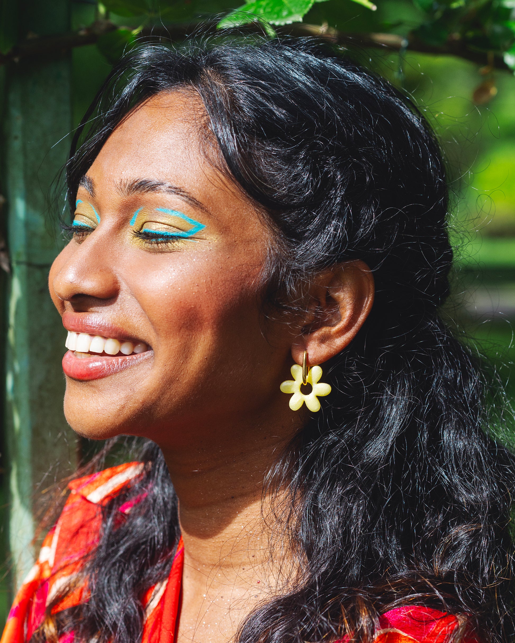 femme indienne de profil souriant, et portant des boucles d'oreilles jaunes en forme de fleur de jasmin en argile polymère faites à la main