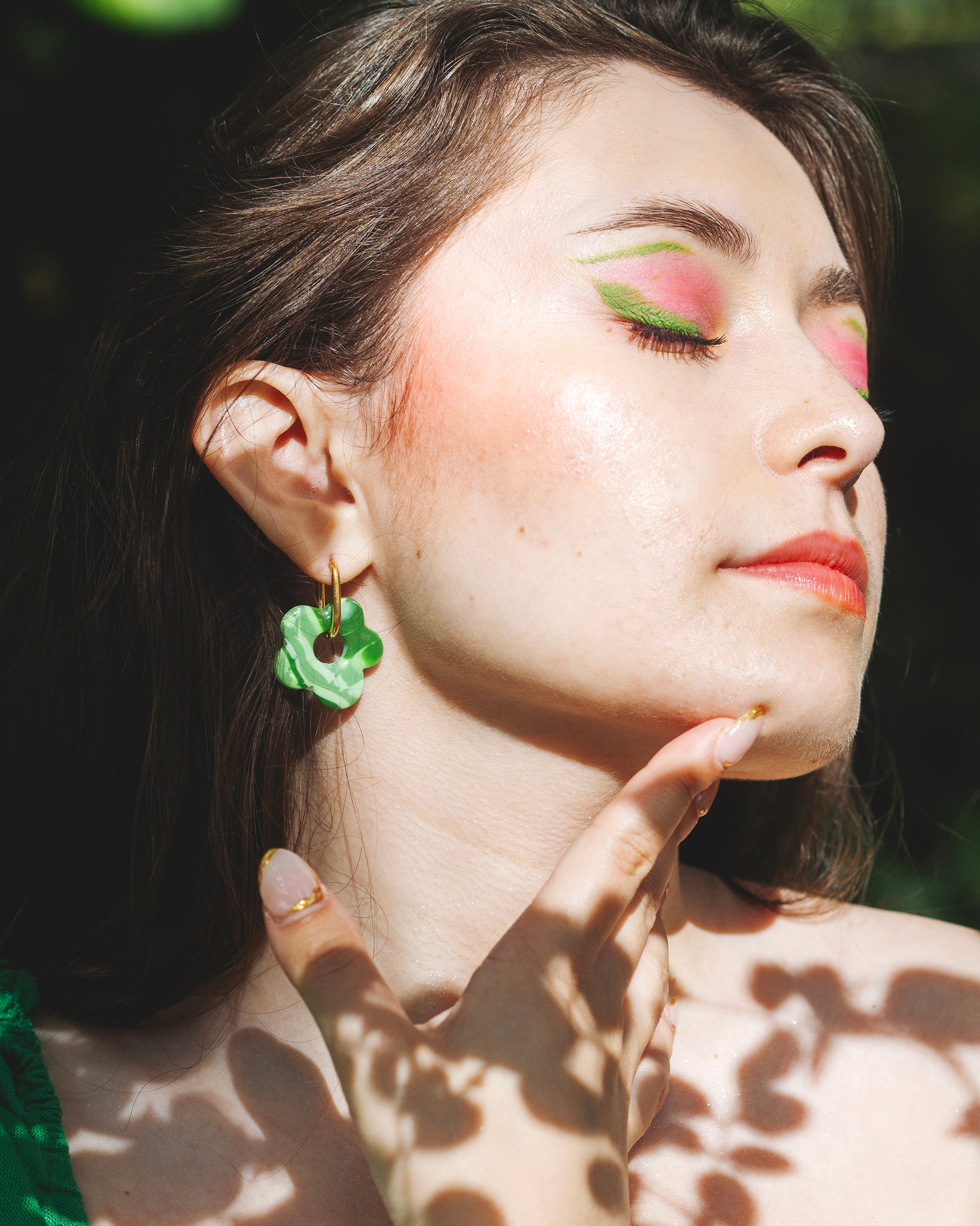 visage de profil de femme se tenant le menton, portant une boucle d'oreille en forme de fleur verte à motifs verts