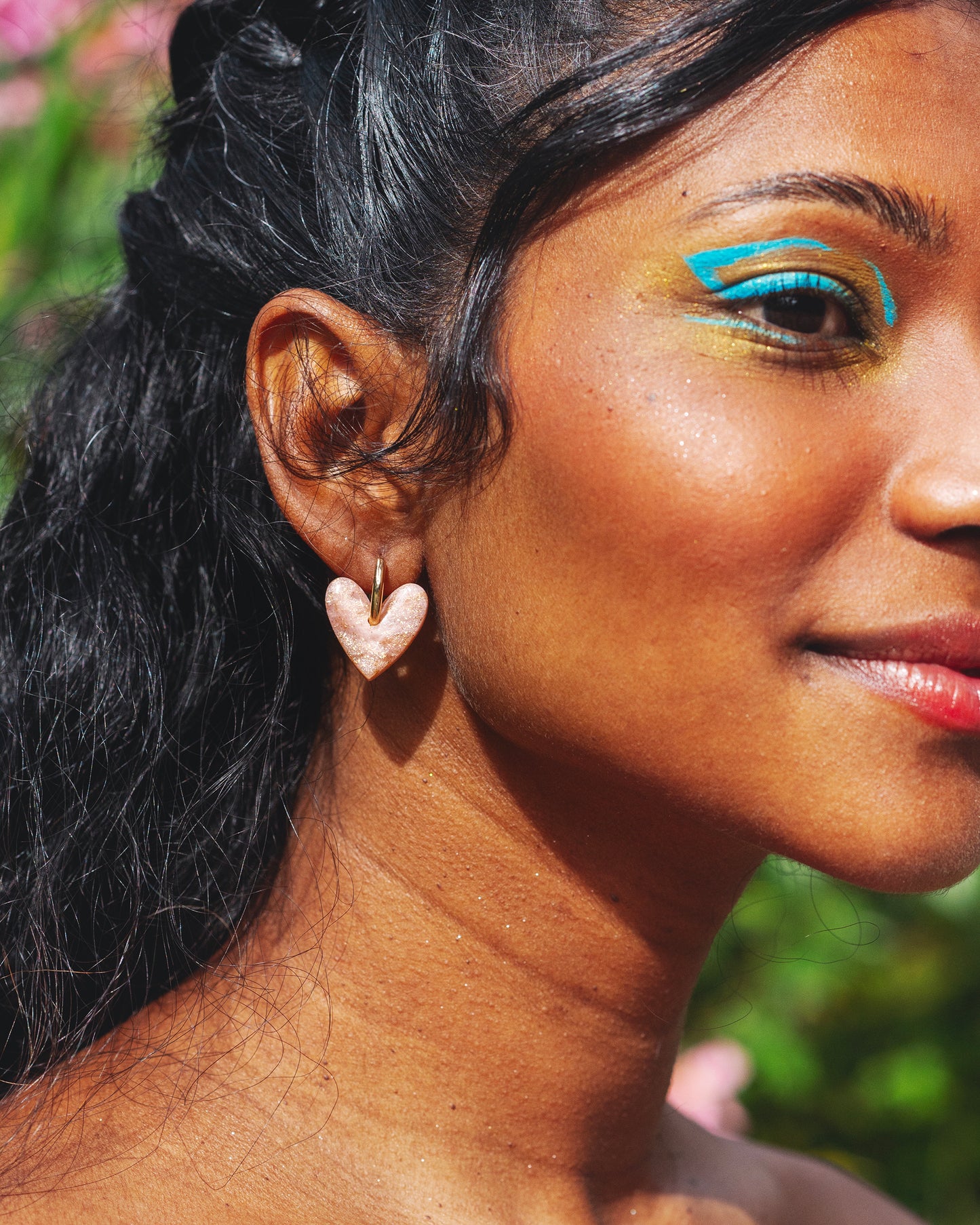 profil du visage d'une femme indienne avec un maquillage coloré turquoise, et portant des boucles d'oreilles fantaisie roses quartz en forme de coeur, faites à la main en argile polymère