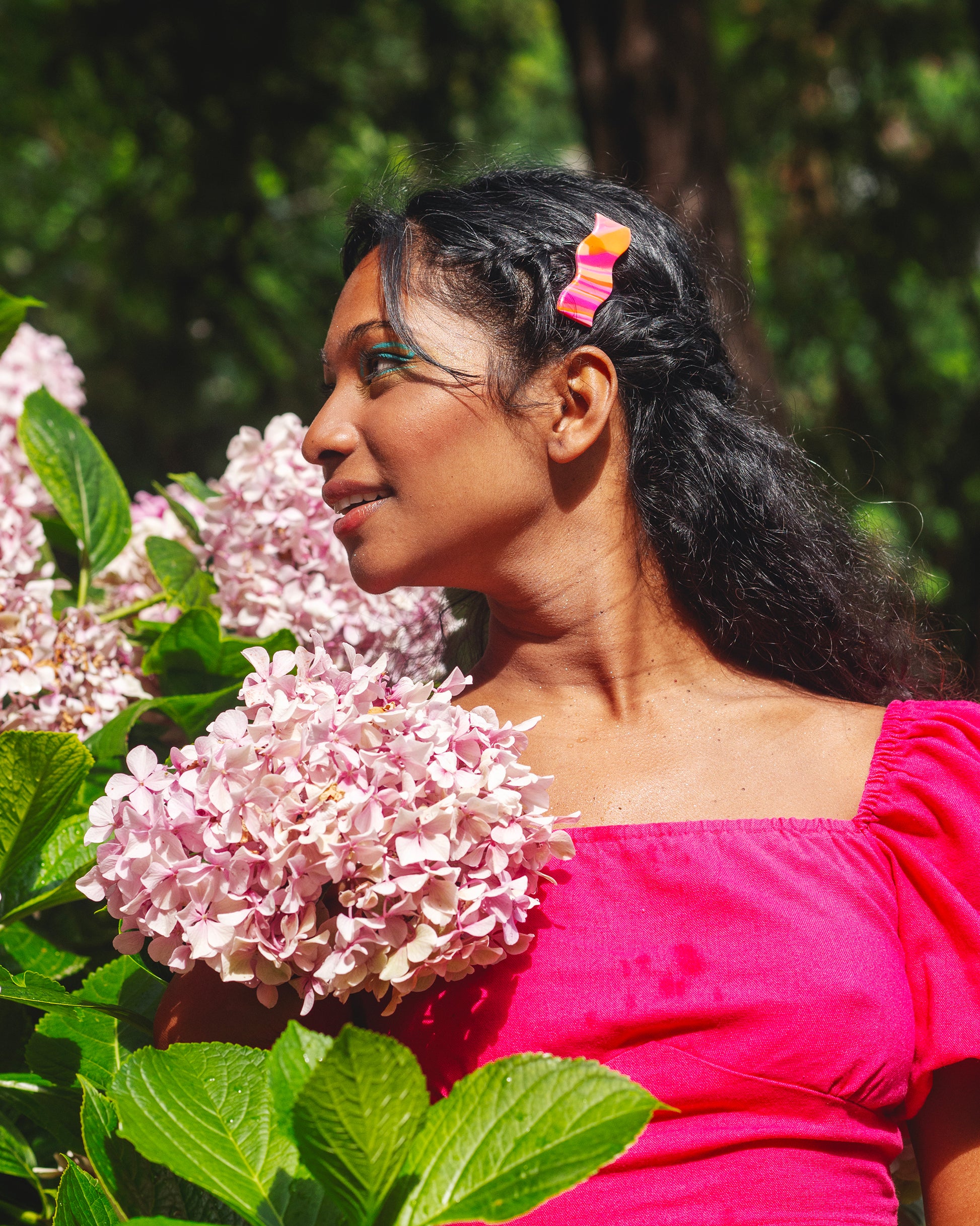 femme indienne de profil portant une barette en argile polymère de forme en vague rose et orange, sur fond d'hortensias roses