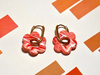 zoom sur deux boucles d'oreilles fantaisie en forme de fleursfaites à la main en argile polymère marbrées roses, avec un anneau rectangulaire doré en acier inoxydable