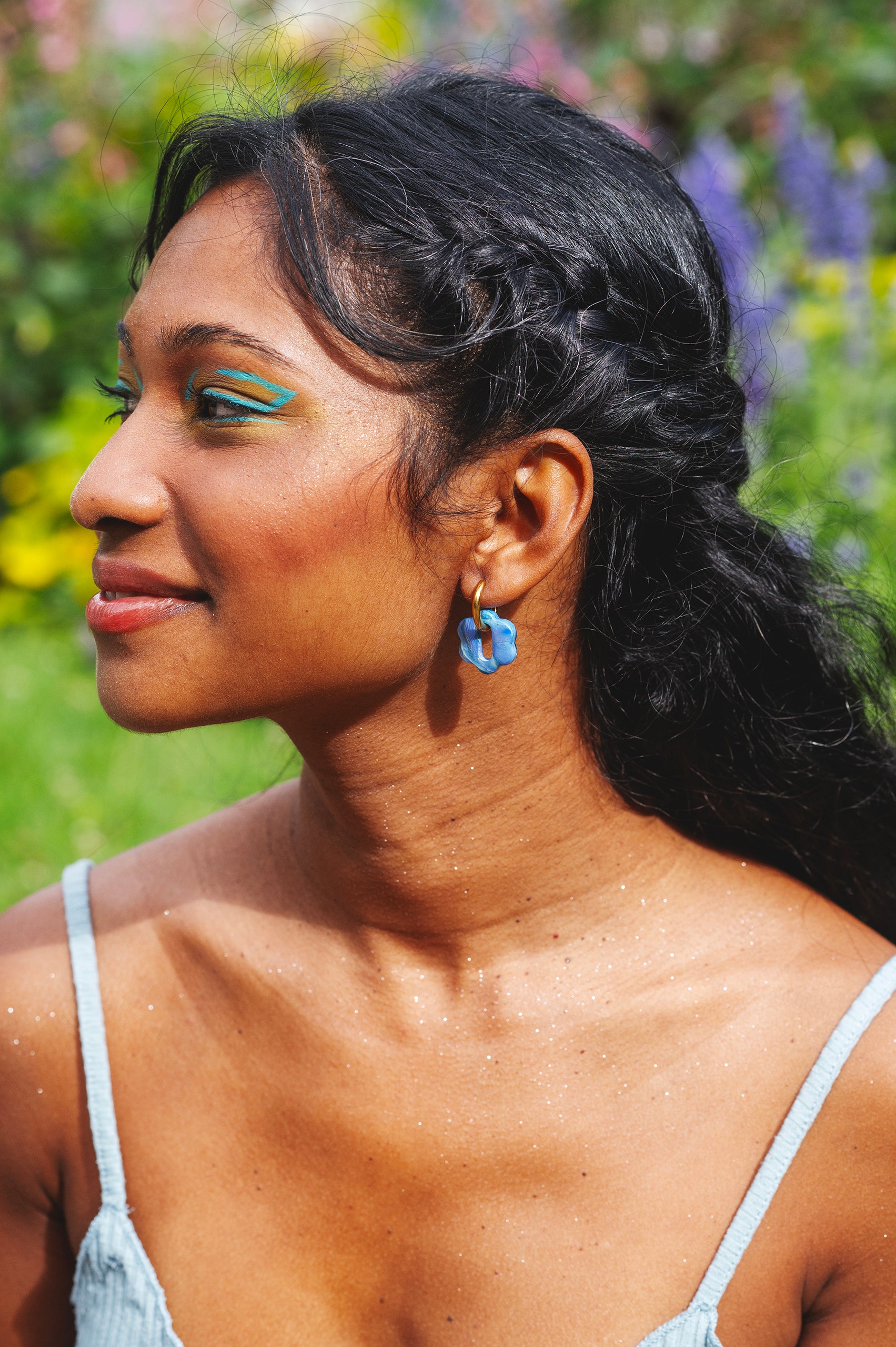 femme de profil indienne qui porte une boucle d'oreille fantaisie en argile polymère faite à la main bleue et dorée avec un anneau rectangulaire en acier inoxydable. la forme est une petite fleur rétro à la fente rectangulaire.