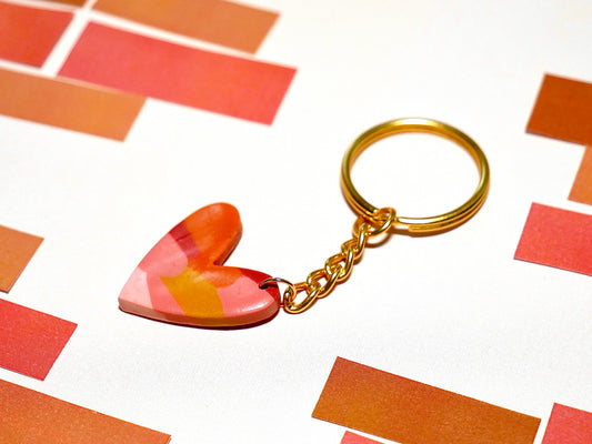 porte-clés fait à la main en argile polymère en forme de coeur de couleur ocre, orange, rouge et rose, sur fond blanc et briquettes