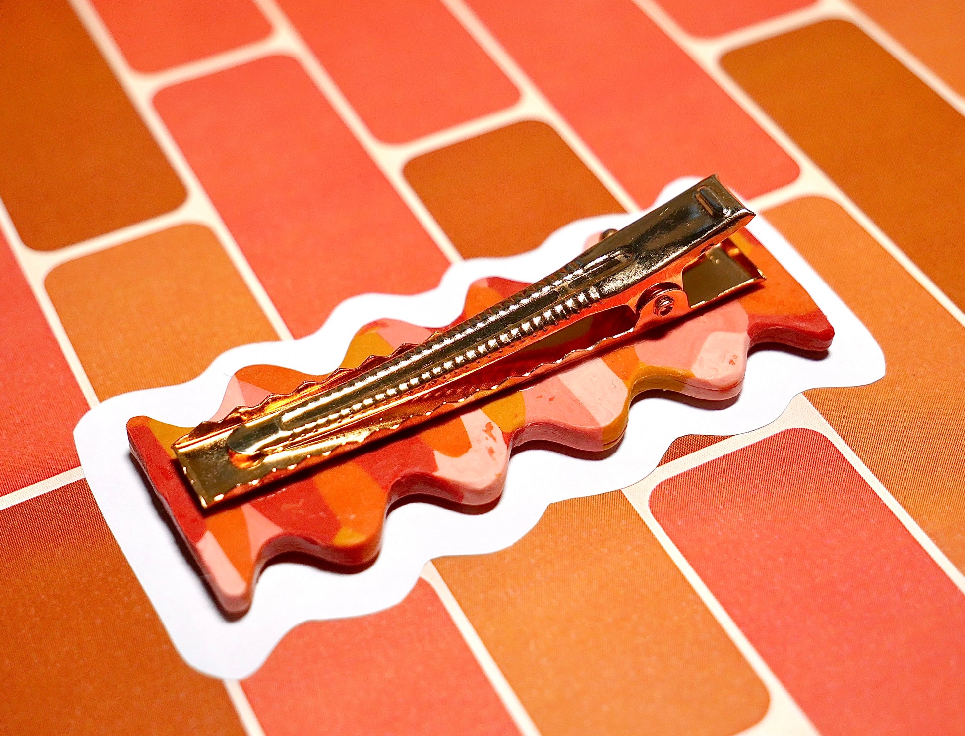 face arrière d'une barrette à cheveux faitesà la main en argile polymèrede forme rétro et groovy de couleur rouge, ocre, terracotta et rose, avec une pince crocodile dorée