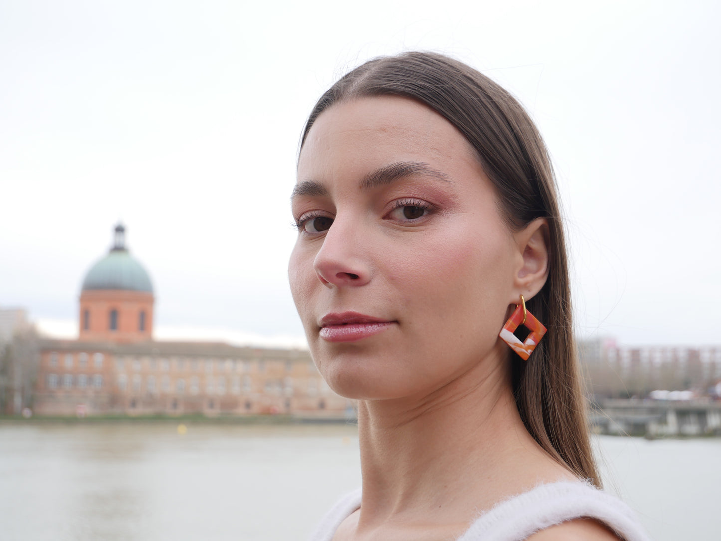 femme regardant la camera de profil devant le Dôme de la Grave à Toulouse, portant une boucle d'oreille en acier inoxydable et un losange en argile polymère