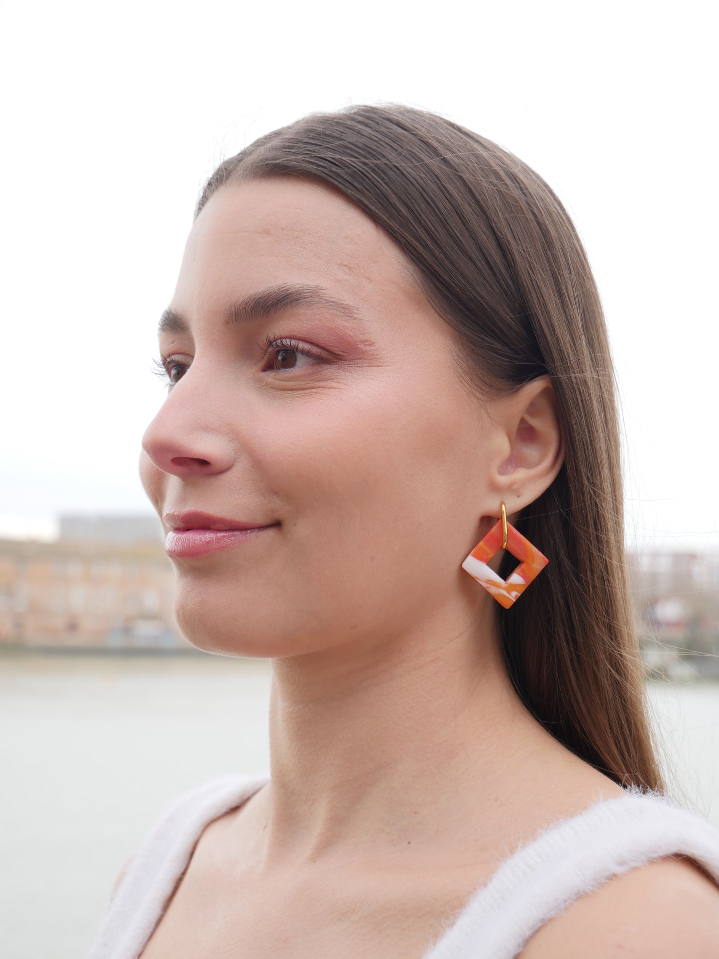 femme de profil souriante devant la Garonne à Toulouse, portant une boucle d'oreille en acier inoxydable et en argile polymère rouge, orange et blanc