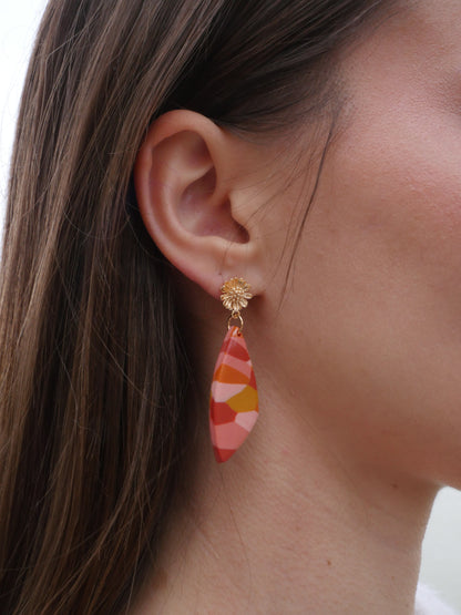 visage de femme de profil avec focus sur son oreilleet portant une boucle d'oreille en argile polymère faite à la main de couleur ocre, terracotta, rose et orange, avec un apprêt en forme de fleur dorée