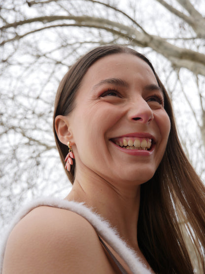 femme souriant et  portant une boucle d'oreille fantaisie aux couleurs rouges et roses dégradées, et divisées en trois parties, le tout en forme de goutte, en argile polymère et faite main