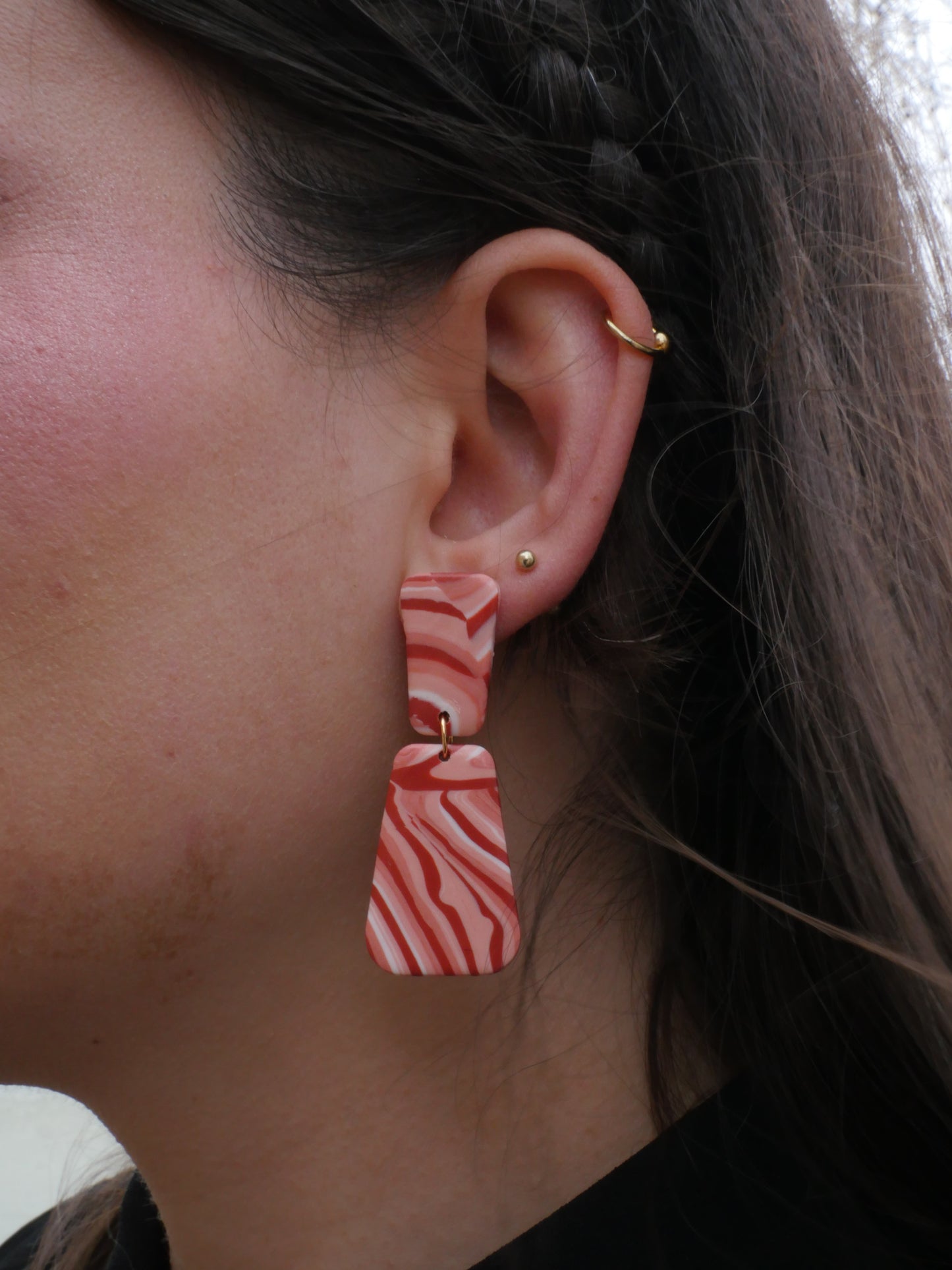 visage de femme de profil portant deux boucles d'oreilles en argile polymère faites à la main au motif de brique, aux couleurs rouge et blanc, constituées de deux trapèze