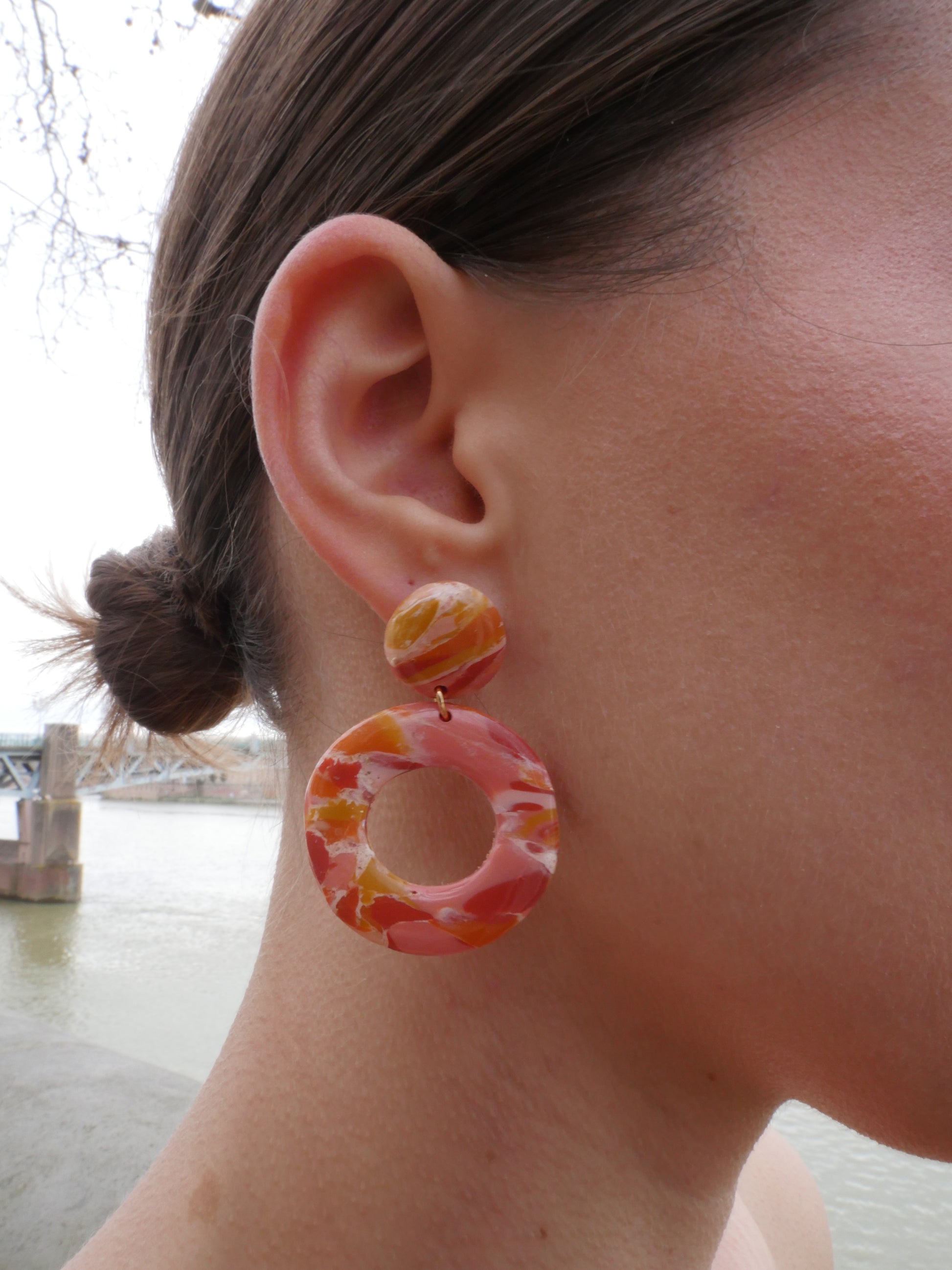 femme de profil qui porte une boucle d'oreille fait main composée d'un rond et un grand cercle marbrés rose, rouge et orange