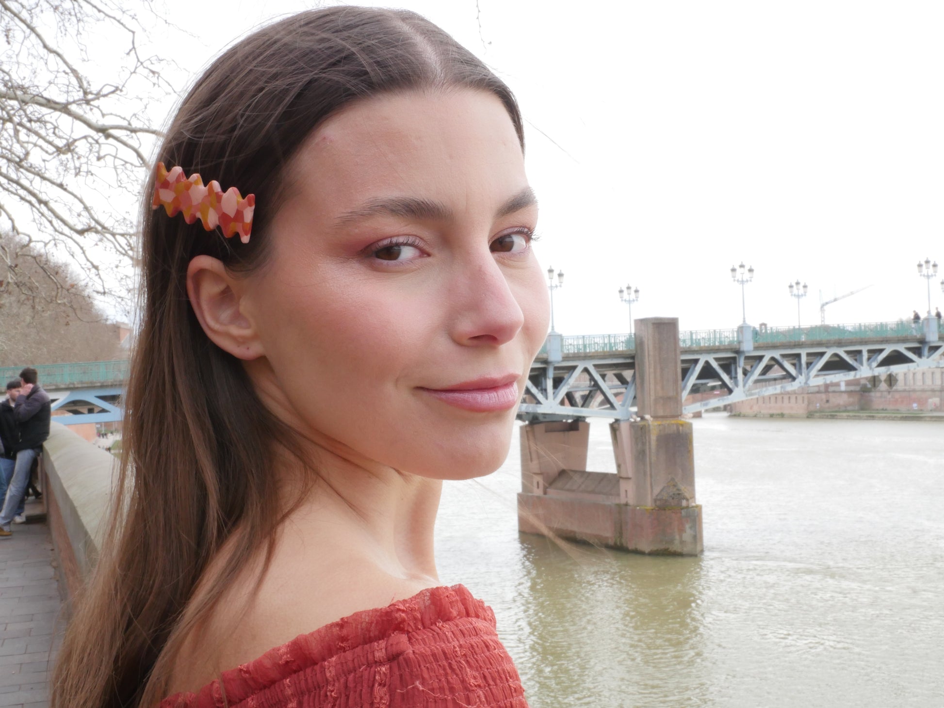 femme devant le Pont Saint Pierre à Toulouse portant une barrette faite à la main en argile polymère de forme rétro et groovy de couleur rouge, ocre, terracotta et rose, avec une pince crocodile dorée