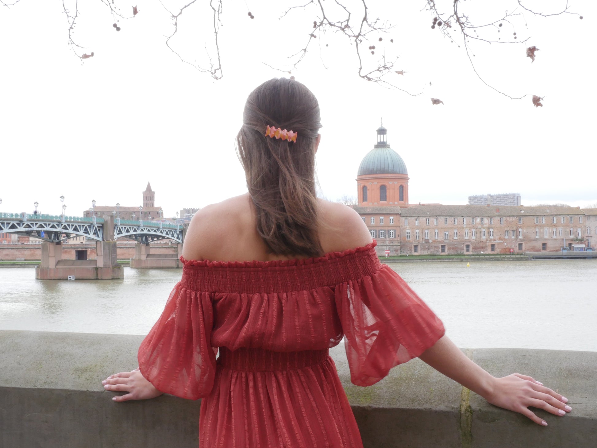 femme de dos face au Dôme de la Grave à Toulouse, portant une barrette à cheveux faitesà la main en argile polymère de forme rétro et groovy de couleur rouge, ocre, terracotta et rose, avec une pince crocodile dorée