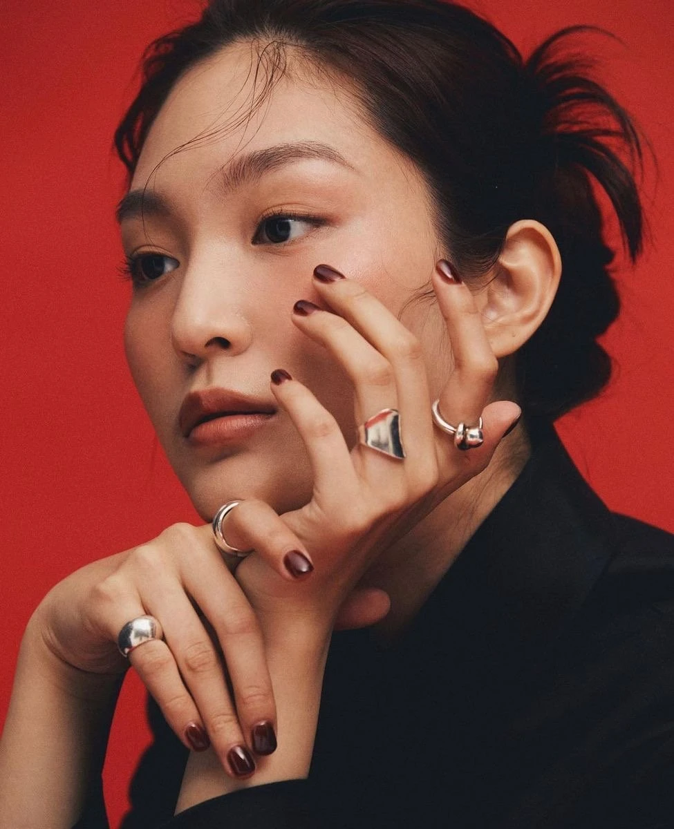 Femme sur fond rouge, portant plusieurs bagues en argent, la main près du visage