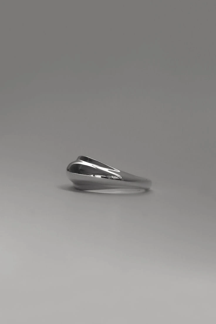 Bague en argent poli aux formes fluides, posée sur fond gris clair
