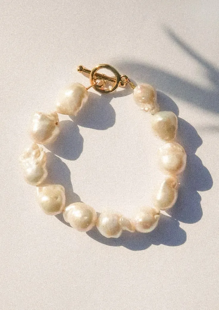 Bracelet de perles baroques blanches à fermoir doré, posé à plat sous une lumière rasante