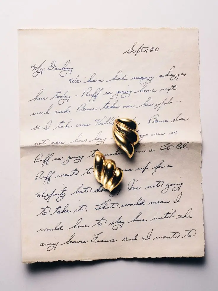 Deux boucles d'oreilles dorées en forme de coquillage posées sur une lettre manuscrite ancienne