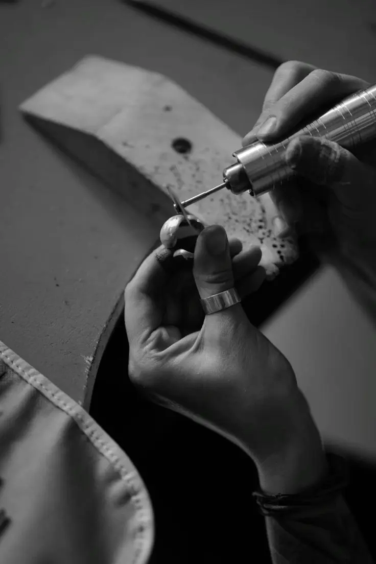 Mains d'artisane travaillant une pièce à l'outil rotatif sur l'établi, en noir et blanc