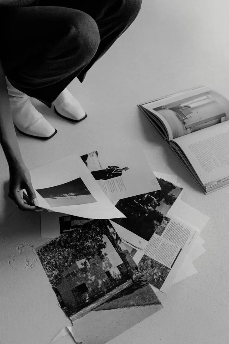 Personne agenouillée disposant des photographies et des magazines ouverts sur le sol, en noir et blanc