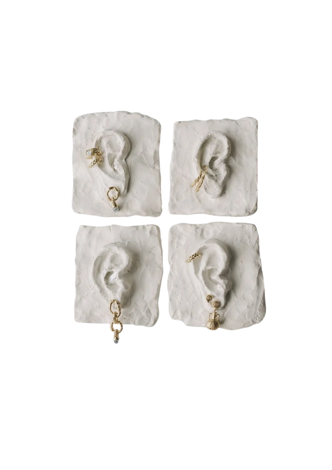 Quatre moulages d'oreilles en plâtre blanc portant des boucles d'oreilles dorées
