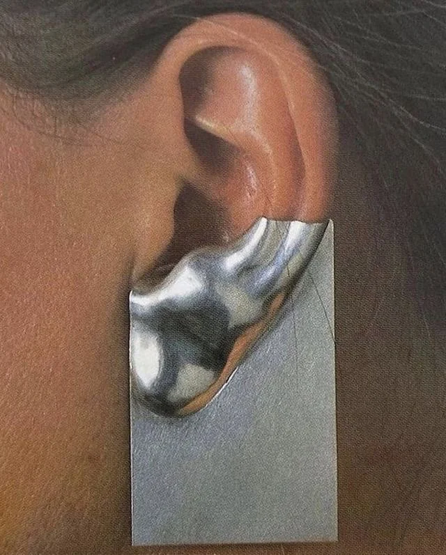 Gros plan d'une oreille portant une boucle rectangulaire en argent au relief bombé