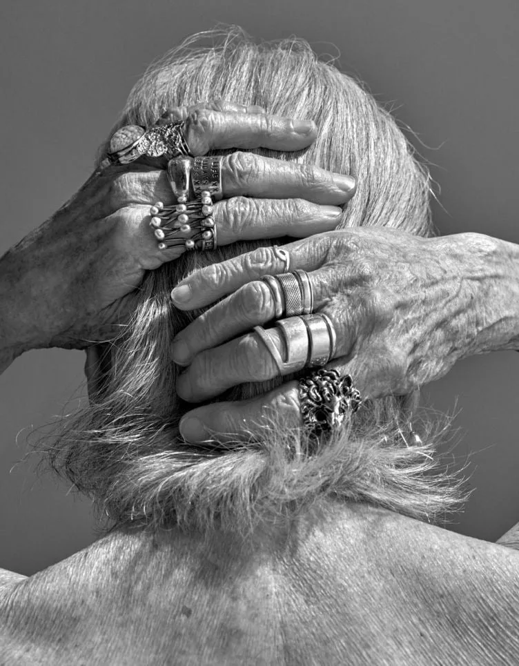 Mains d'une femme âgée aux nombreuses bagues en argent, posées sur ses cheveux gris, de dos
